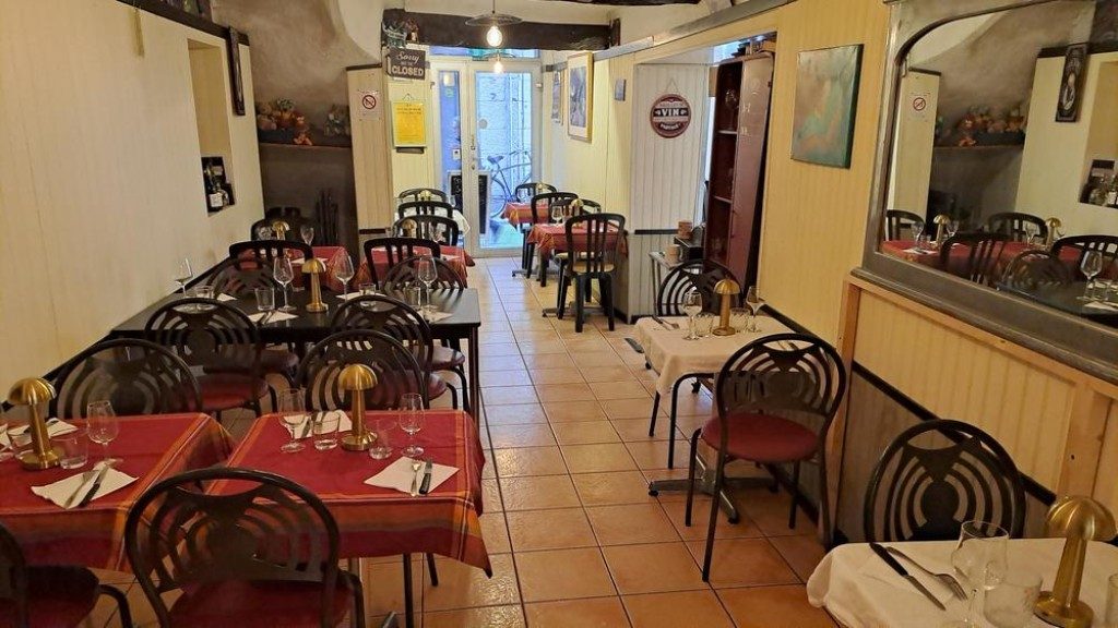 La salle du restaurant : tables aux nappes rouges et chaises noires, murs clairs et carrelage de terre cuite