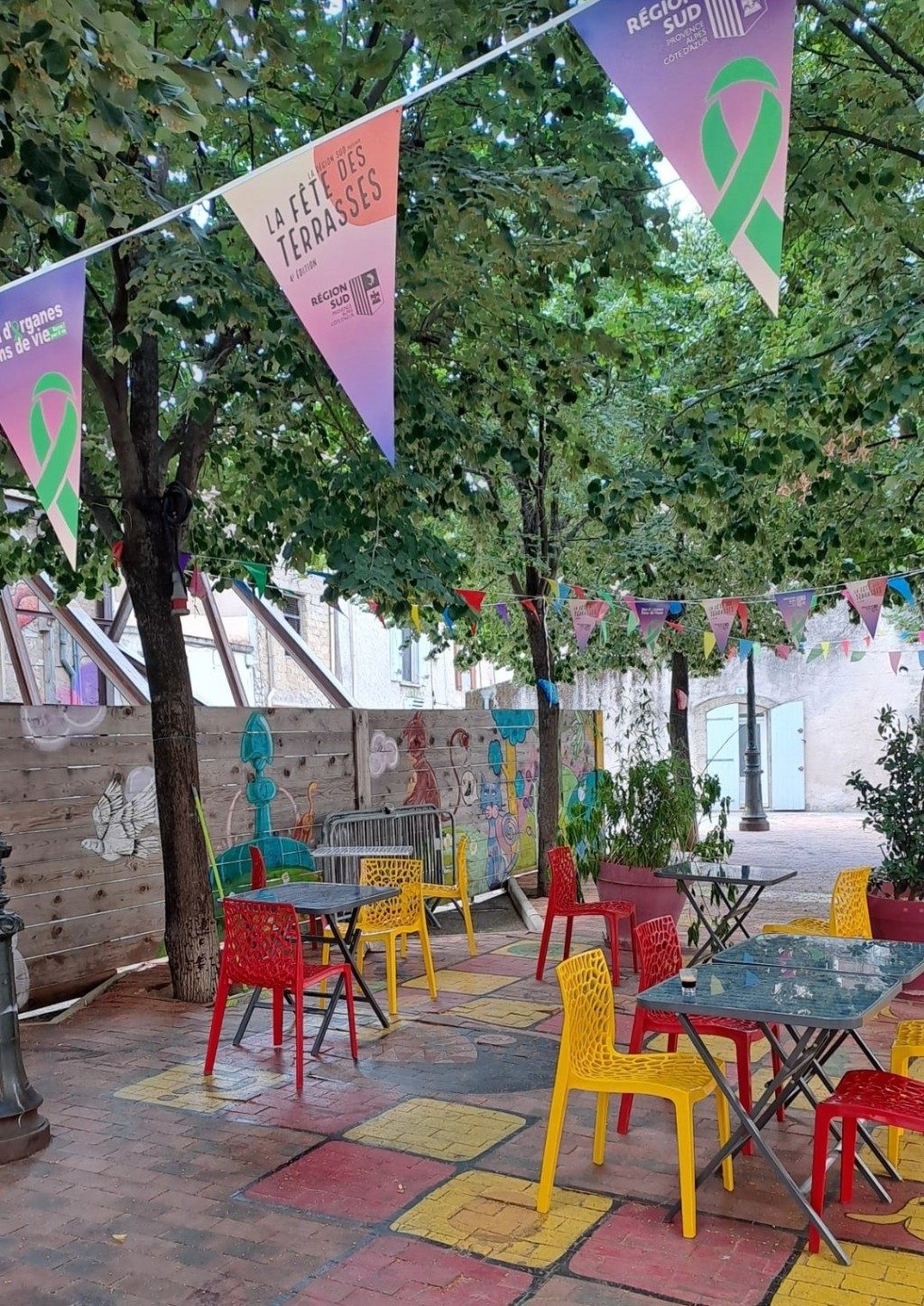 La terrasse sous les tilleuls : fanions colorés, tables et chaises jaunes, rouges et turquoise