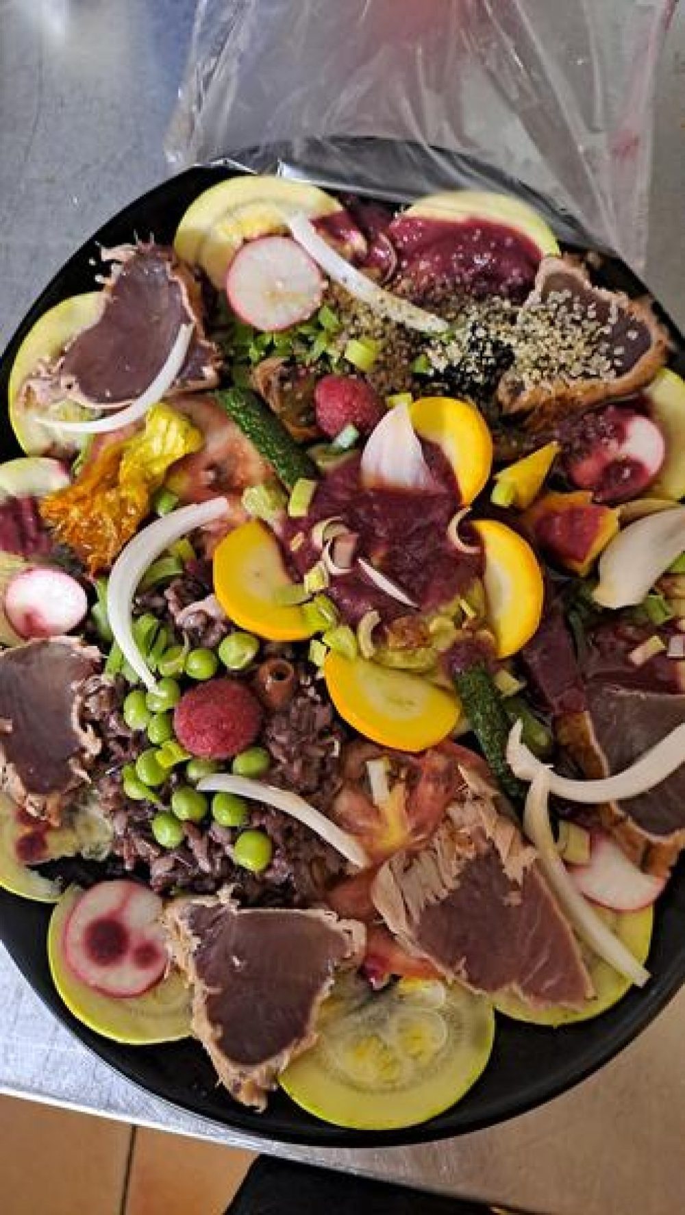 Une assiette de thon mi-cuit en tranches, avec des légumes, des fleurs et des graines